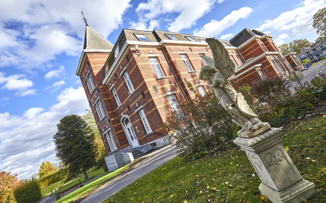 Bâtiment de l'Institut Notre-Dame des Anges en briques rouges avec un toit pointu et une statue d'ange en premier plan sur la gauche