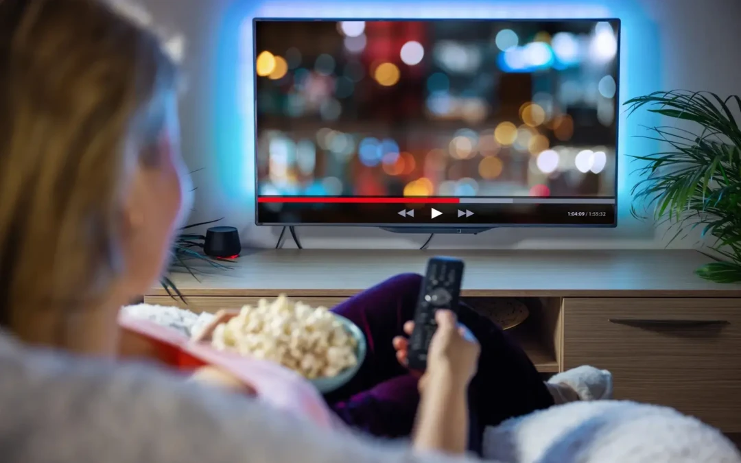 Femme regardant une télévision connectée avec une interface de streaming, illustrant l’IPTV et la vidéo à la demande (VOD) pour une expérience immersive de divertissement à domicile.