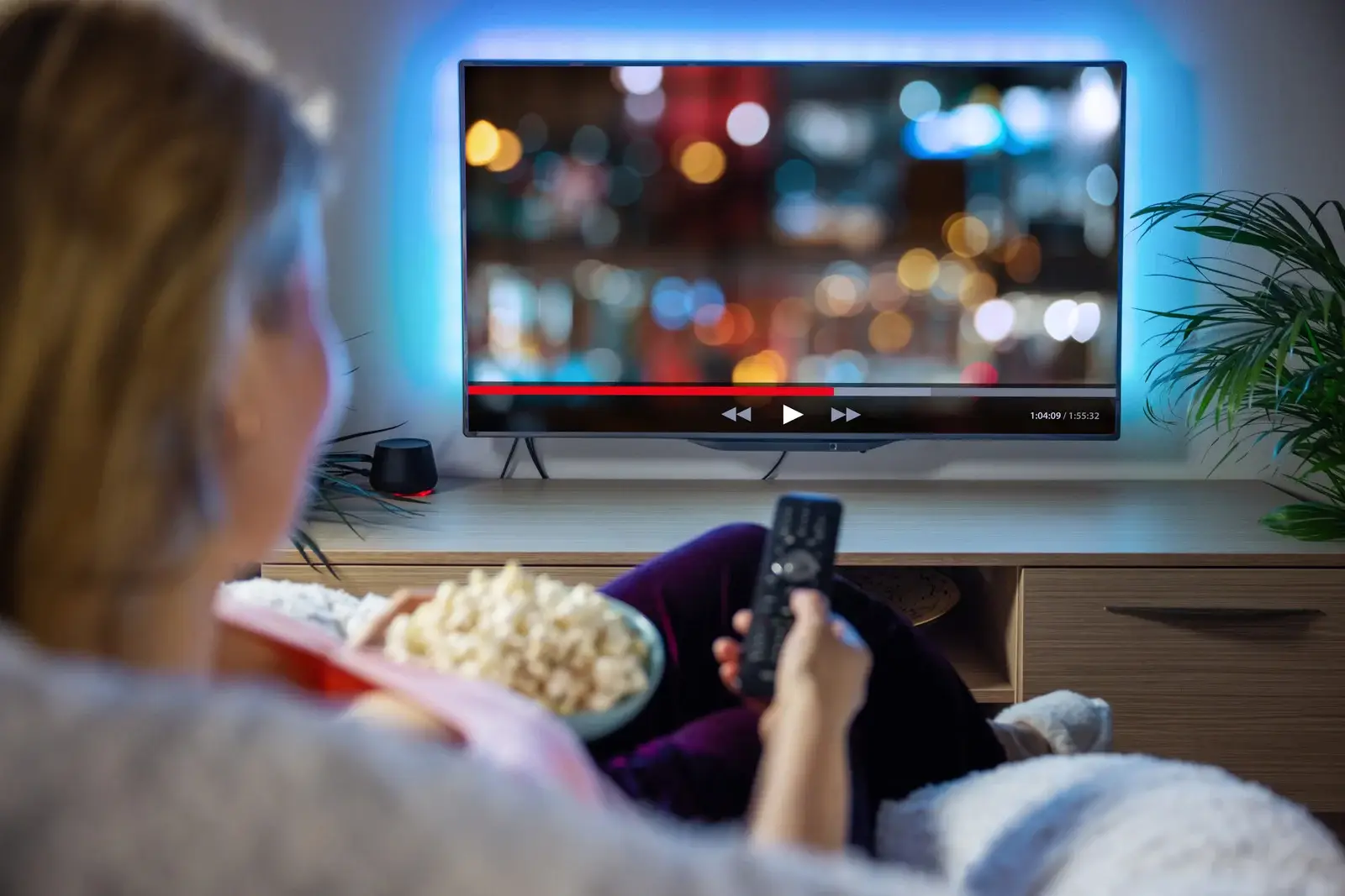 Femme regardant une télévision connectée avec une interface de streaming, illustrant l’IPTV et la vidéo à la demande (VOD) pour une expérience immersive de divertissement à domicile.