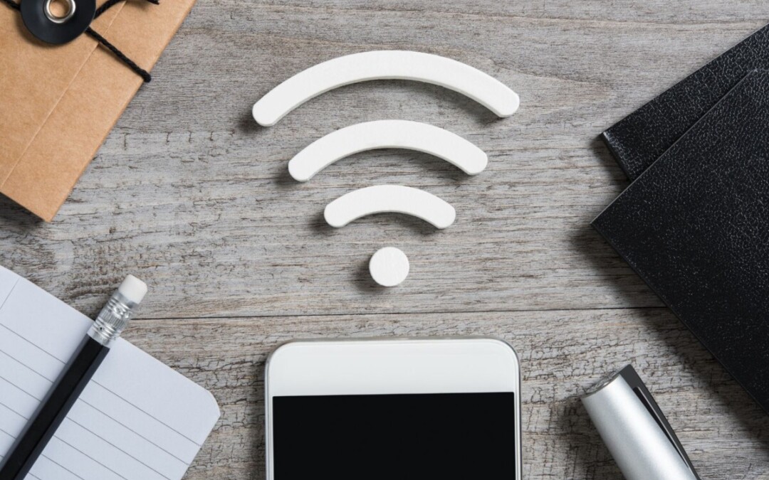 Gros plan sur un bureau avec un agenda, un carnet de notes, un smartphone, un stylo et un livre. Au milieu de l'image, on peut voir le symbole représentant la connexion Wifi, représentant l'accès au Wifi dans une résidence étudiante.