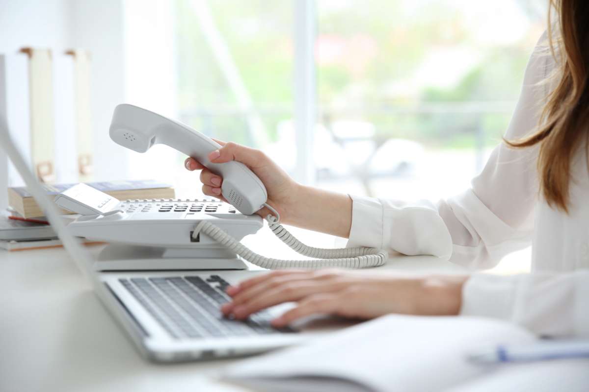 Femme assise à un bureau devant son ordinateur en train de prendre son téléphone à technologie VOIP