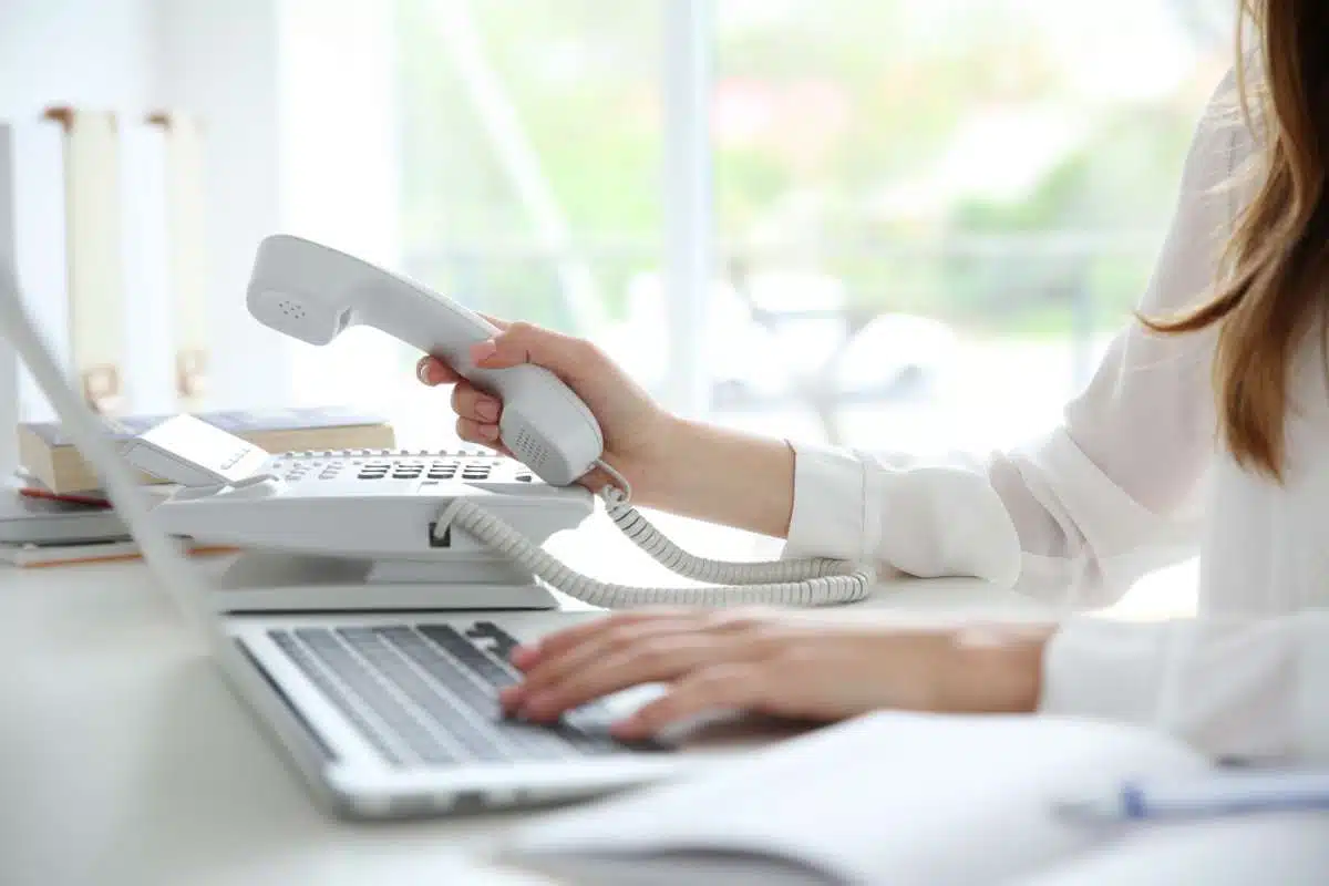 Femme assise à un bureau devant son ordinateur en train de prendre son téléphone à technologie VOIP