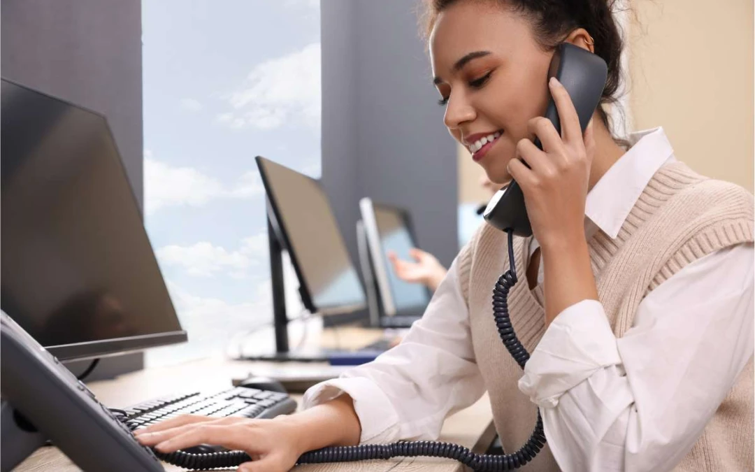 Femme assise à son bureau et passant un coup de téléphone en souriant