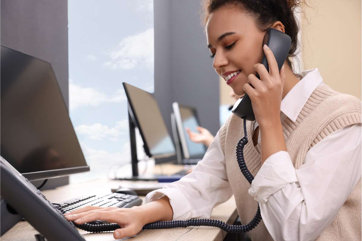 Femme assise à son bureau et passant un coup de téléphone en souriant