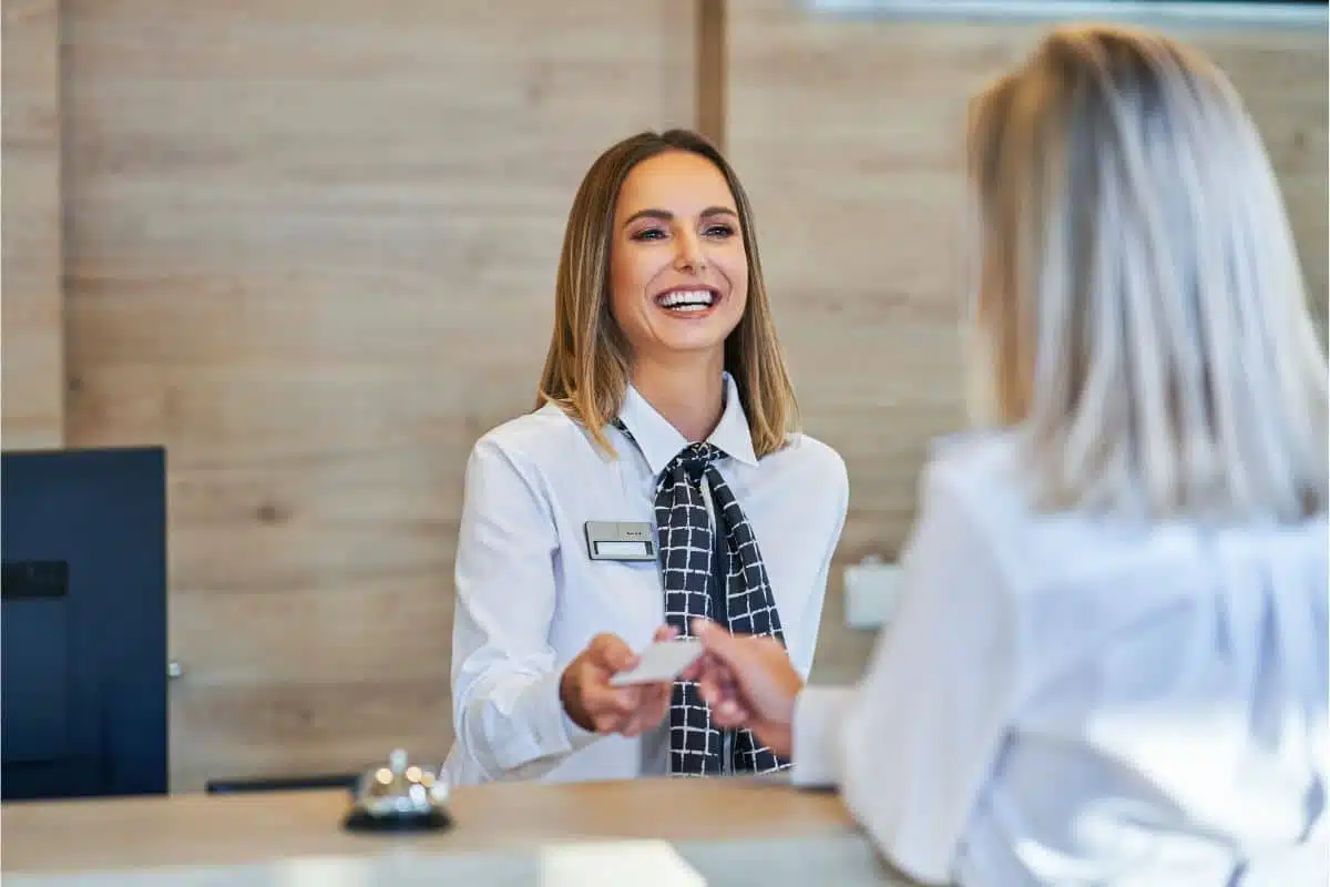 ac-it-receptionniste-hotel-connecte Réceptionniste souriante d'un smart hôtel qui tend une carte de chambre à une cliente