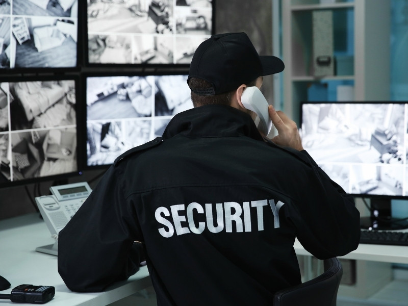 Homme de la sécurité de dos observant des écrans de caméra vidéosurveillance dans un centre commercial