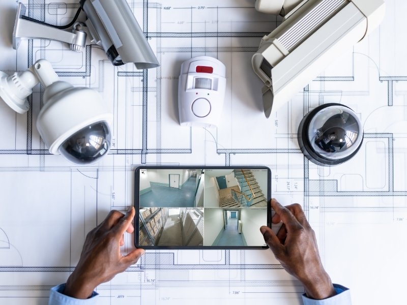 Différentes caméras de vidéosurveillance avec un homme tenant une tablette visionnant les pièces filmées